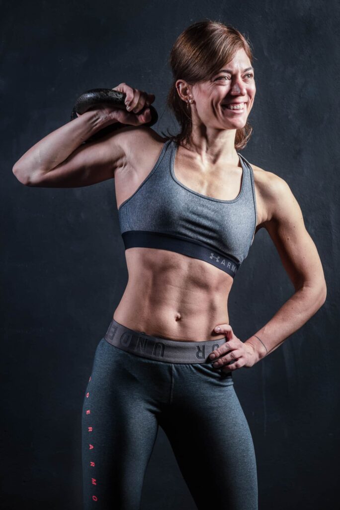 fotografofitness ragazza personal trainer sorridente con addome scolpito mentre tiene in mano un kettlebell